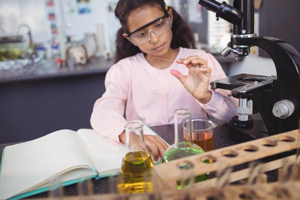 Día internacional de la mujer y la niña en la ciencia: Niña trabajando con instrumentos de laboratorio (probetas, microscópio, libro de notas, etc.).